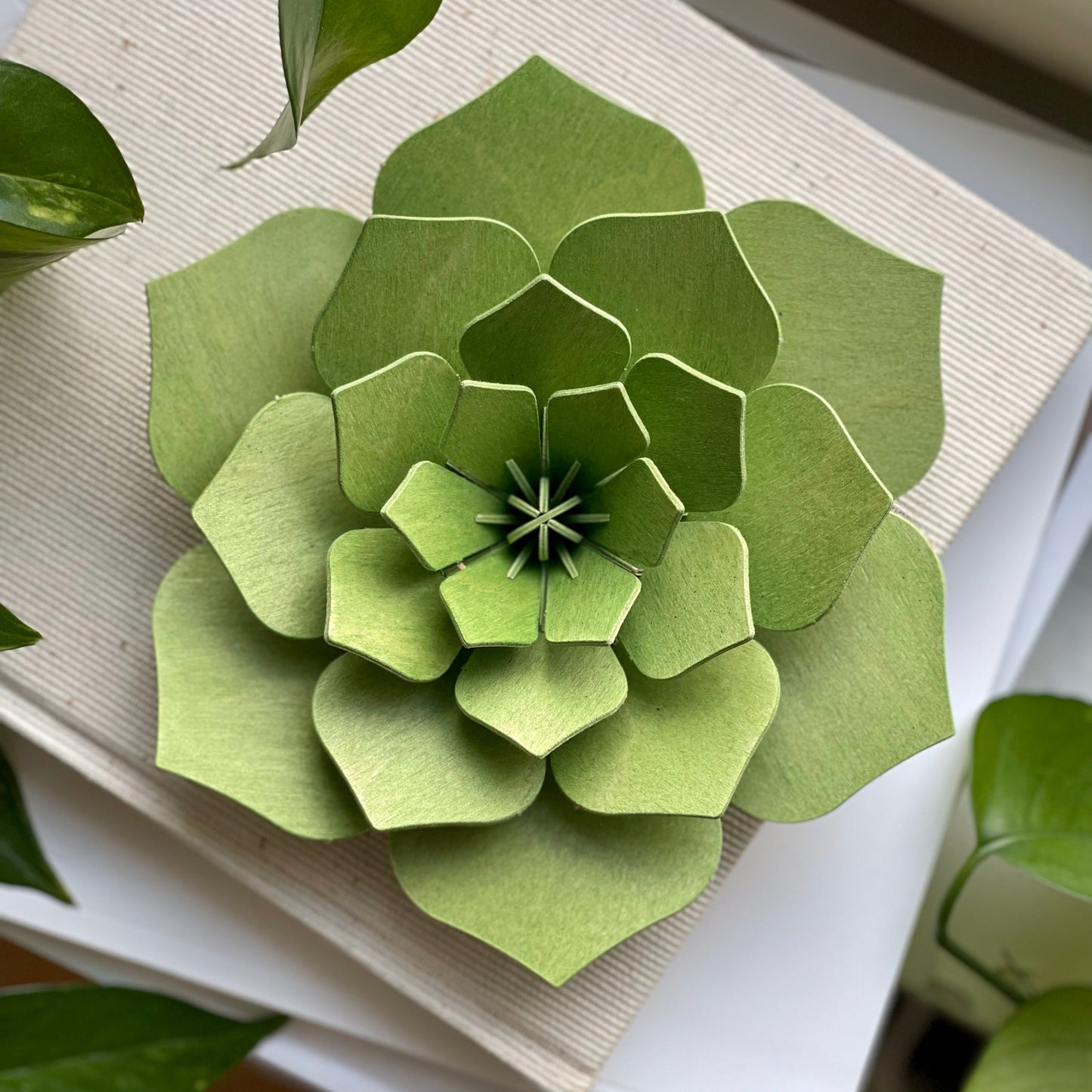 Green paper flower sculpture on a white surface with green leaves in the background