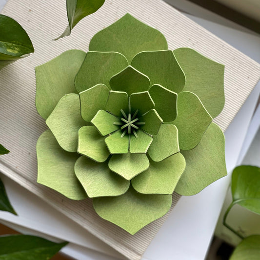 Green paper flower sculpture on a white surface with green leaves in the background